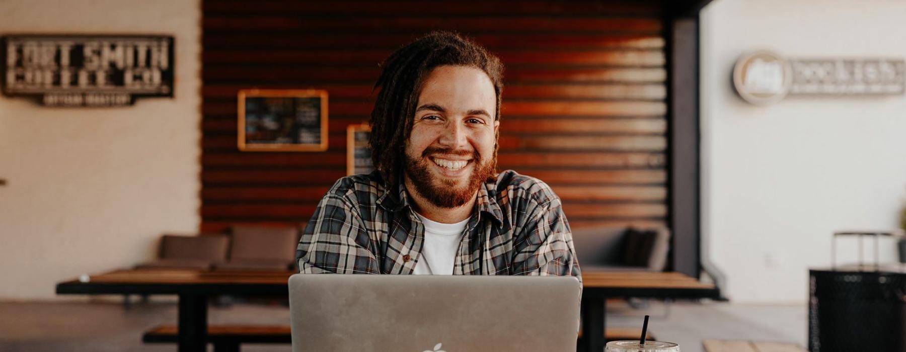 man sits with a drink in front of an open laptop in local restaurant