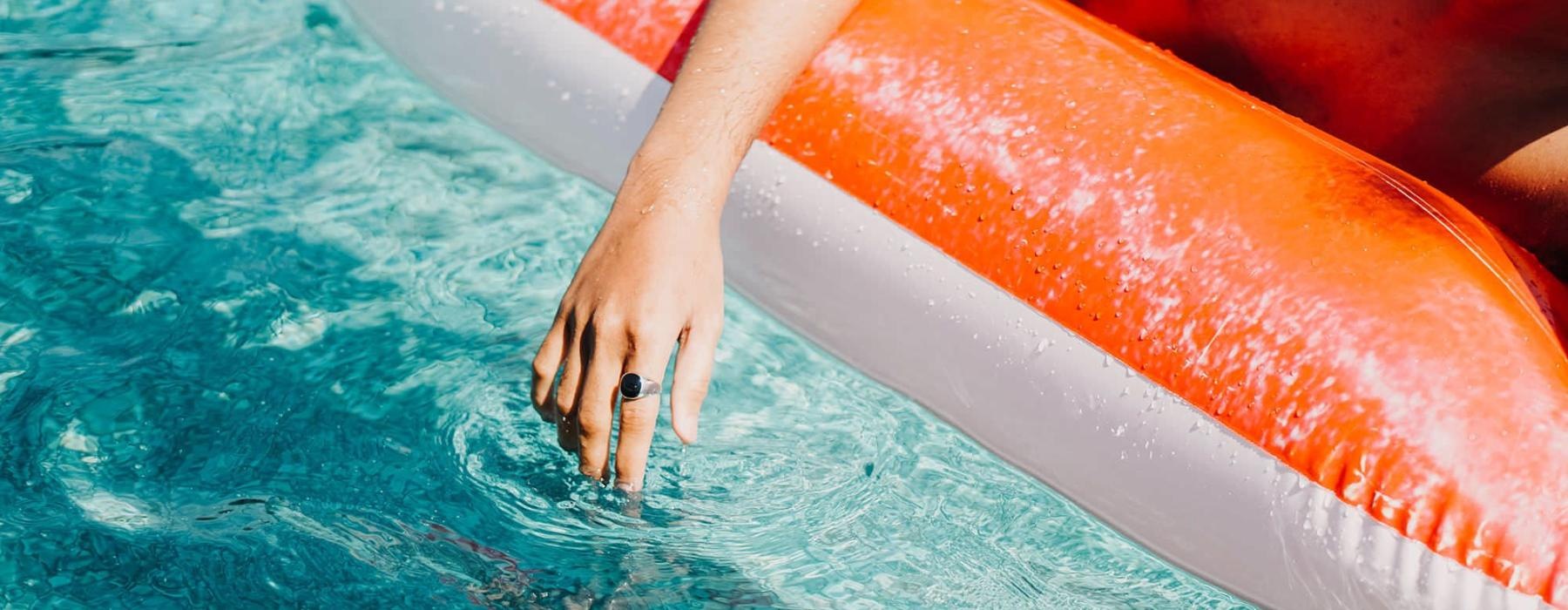 woman dangles her hand in the pool as she floats in an inflatable vessel